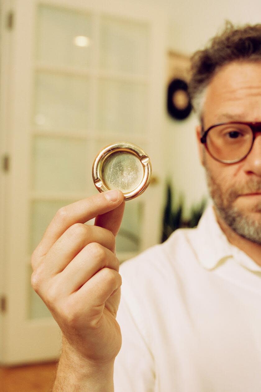 Seth Rogen holds up a small circular ashtray.