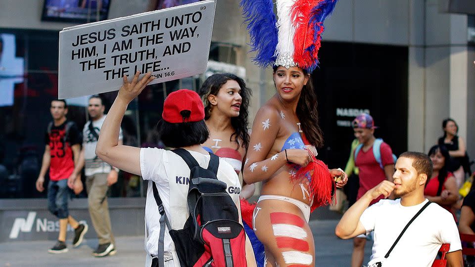 A proselytiser walks by two women clad in thongs and body paint in Times Square, in New York. Photo: AP/Julie Jacobson