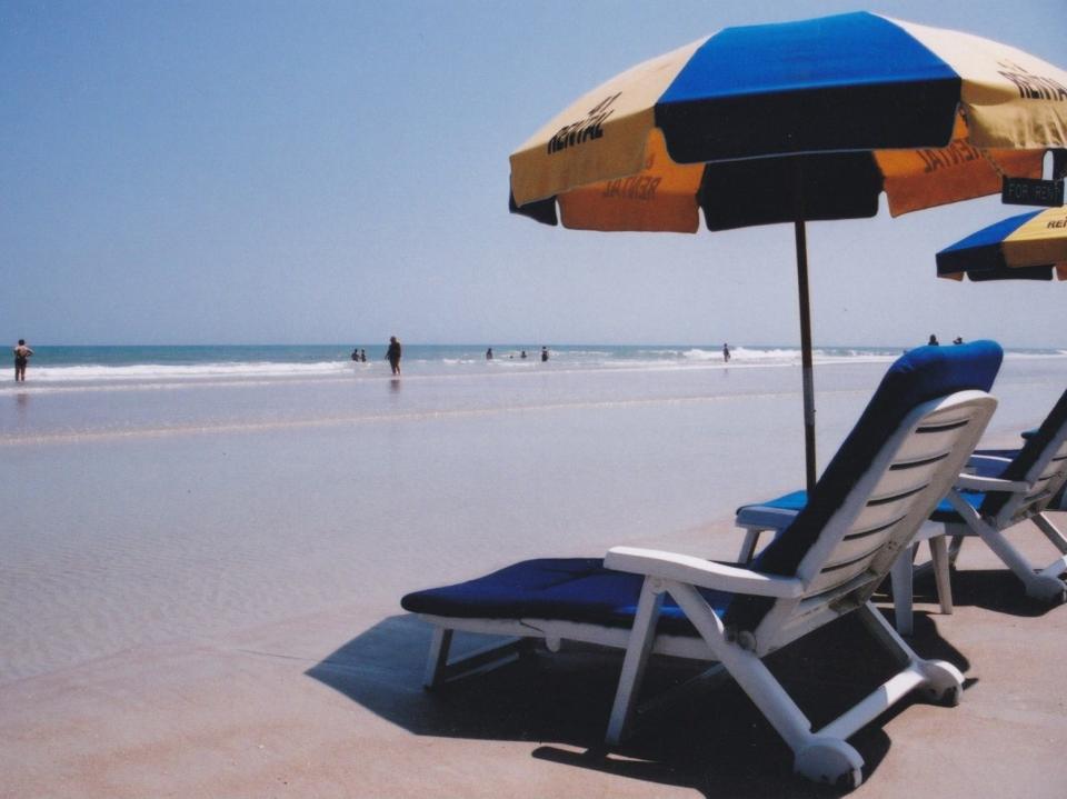 A yellow and blue beach umbrella next to a loungechair on the beach.