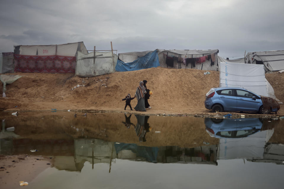 Palestinians displaced by the Israeli ground offensive on the Gaza Strip walk through a flooded makeshift tent camp in Rafah, Gaza Strip, Sunday, Feb. 18, 2024. (AP Photo/Mohammed Dahman)