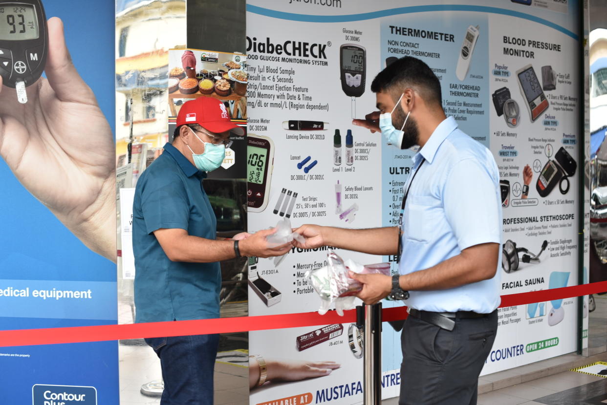 A security guard hands out disposable gloves to a man outside the supermarket section of the Mustafa Center on Saturday, May 16, 2020 in Singapore’s Little India district. Singapore has reported more than 27,000 COVID-19 cases, with 90% of the cases linked to foreign workers dormitories, but it has a low fatality rate of 21 deaths. (AP Photo/YK Chan)