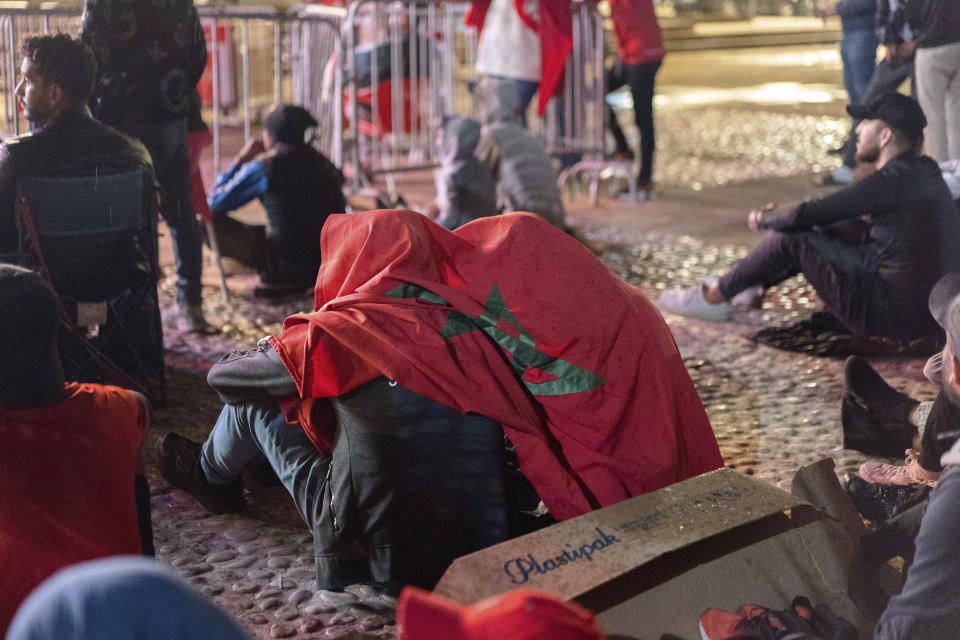 Moroccans draped in the country flag to shelter from rain react as they watch the World Cup semifinal soccer match between France and Morocco played in Qatar, at a public viewing place in Rabat, Morocco, Wednesday, Dec. 14, 2022. (AP Photo/Sonia Moussaid)