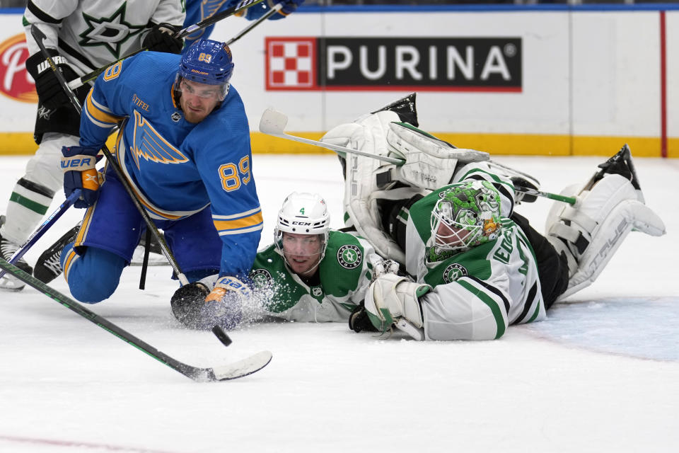 Dallas Stars goaltender Scott Wedgewood, right, Miro Heiskanen and St. Louis Blues' Pavel Buchnevich (89) reach for a loose puck during the second period of an NHL hockey game Saturday, Dec. 16, 2023, in St. Louis. (AP Photo/Jeff Roberson)