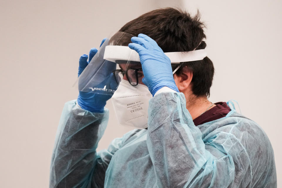 A technician wearing blue scrubs and blue nitrile gloves adjusts his plastic visor over his glasses.