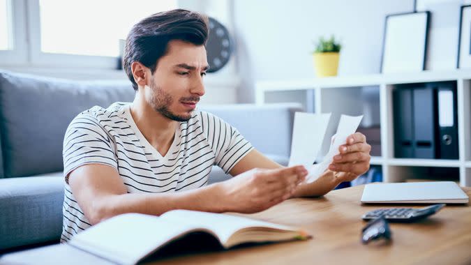 Unhappy man looking at bills sitting at table in living room.