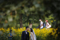 People wearing face masks to help curb the spread of the coronavirus pass by a newly weds kissing as they posing for wedding photos at the Olympic Forest Park in Beijing, Thursday, July 2, 2020. China reported three new cases of coronavirus, including just one case of local transmission in the capital Beijing, appearing to put the country where the virus was first detected late last year on course to eradicating it domestically, at least temporarily. (AP Photo/Andy Wong)