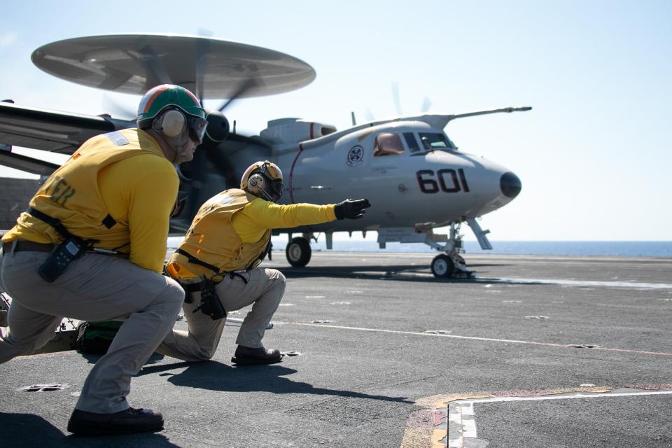 Two people in yellow uniforms and protective headwear kneeling with a helicopter behind them.