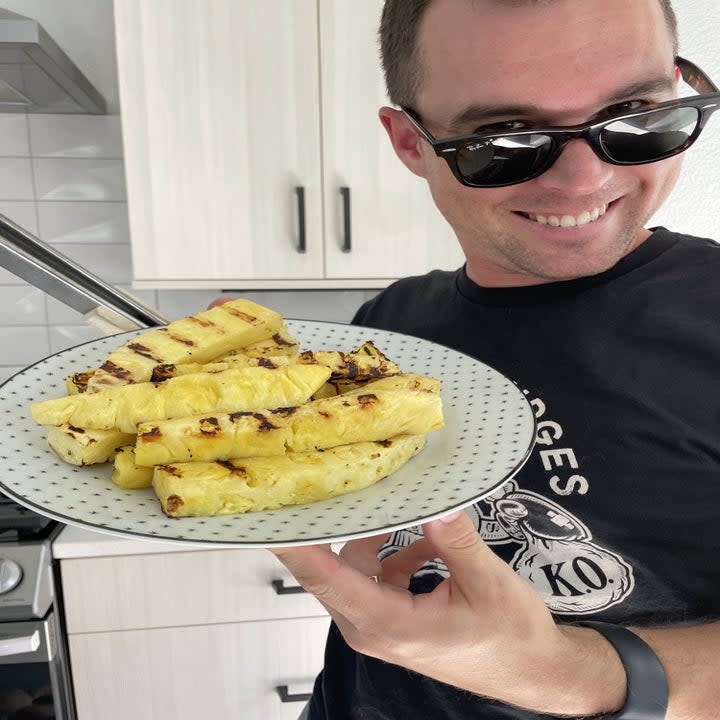author's husband holding a plate of grilled pineapple