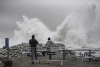 Two people watch the waves hitting the breakwater in Barcelona, Spain, Wednesday, Jan. 22, 2020. Massive waves and gale-force winds smashed into seafront towns, damaging many shops and restaurants and flooding some streets. (AP Photo/Joan Mateu)