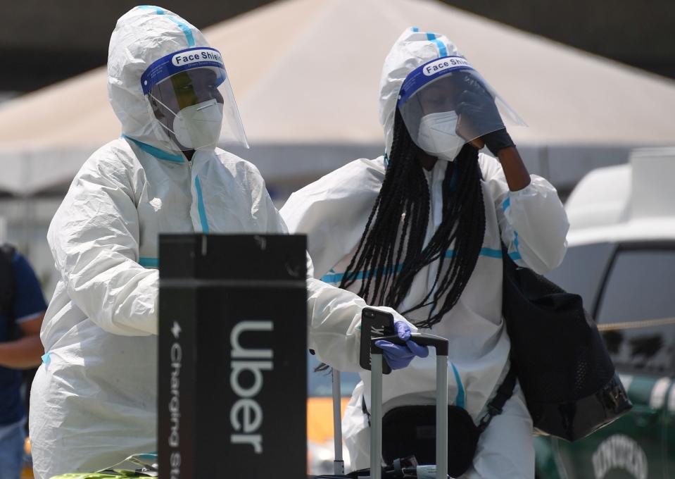 uber covid travel Travelers wearing protective suits, facemasks, face shields and gloves walk past an Uber pick up area August 20, 2020 at Los Angeles International Airport in Los Angeles, California. - Rideshare service rivals Uber and Lyft were given a temporary reprieve on August 20 from having to reclassify drivers as employees in their home state of California by August 21. (Photo by Robyn Beck / AFP) (Photo by ROBYN BECK/AFP via Getty Images)