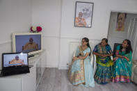 Aagna Patel, 16, Pushpa Patel, 68, Hemali Patel 42, dressed in their best saris, watch Guru Pujya Swayamprakashdas speak to them through their television screen in the comfort of their living room in their suburban home in Hemel Hempstead, England, on Sunday, June 14, 2020. "That is what we would have worn to the temple," said Hemali, "so it felt only right to dress for the occasion." (AP Photo/Elizabeth Dalziel)