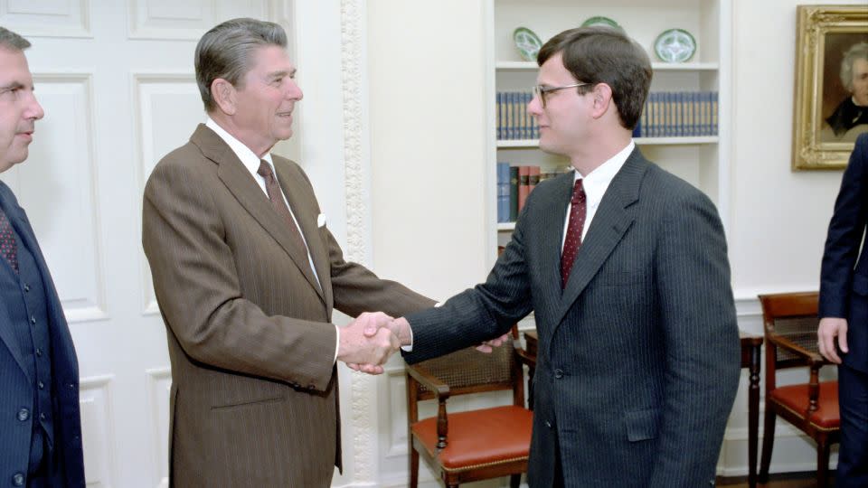 In this January 1983 photo, President Ronald Reagan greets John Roberts during a photo opportunity with members of the White House Counsel's Office in the Oval Office in Washington, DC. - US National Archives and Records Administration
