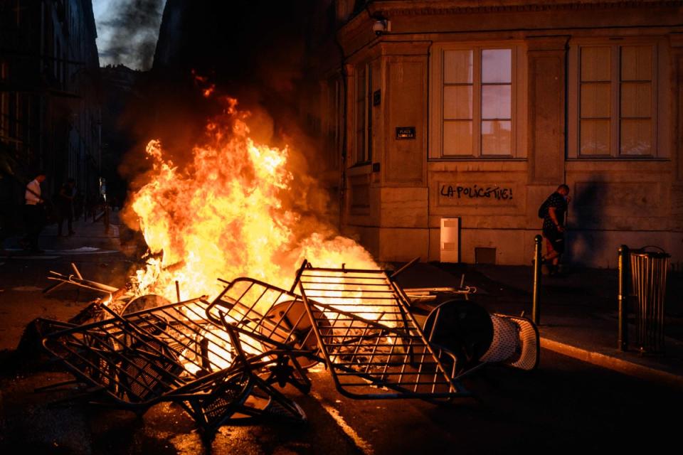 A woman walks past a wall lit up by a nearby fire on which it is written, 'Police kill', during clashes with police in Lyon on Friday (AFP via Getty Images)