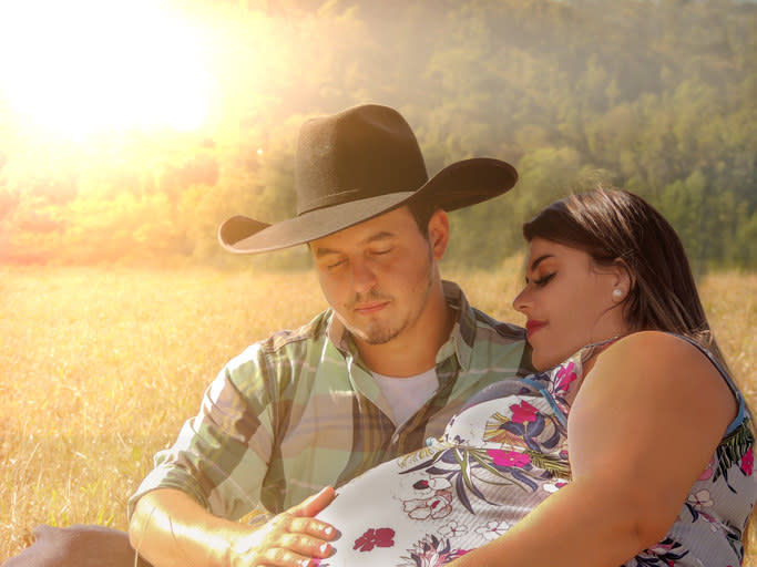 a cowboy holds a hand over a pregnant person's belly