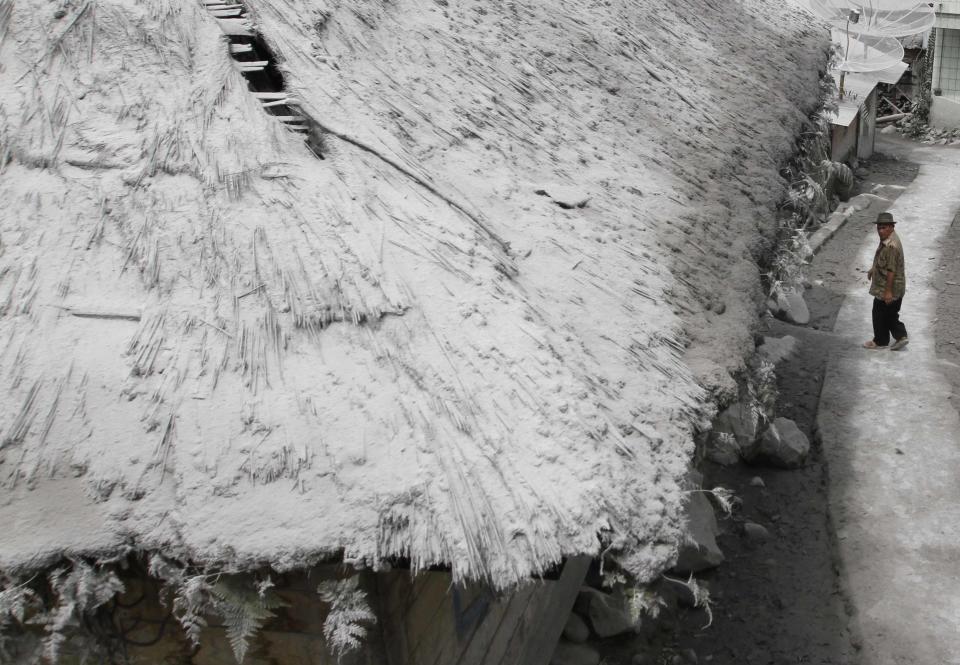 Man walks on road near ash-covered roof in empty village after all villagers were evacuated after Mount Sinabung spewed ash at Mardingding village in Karo district