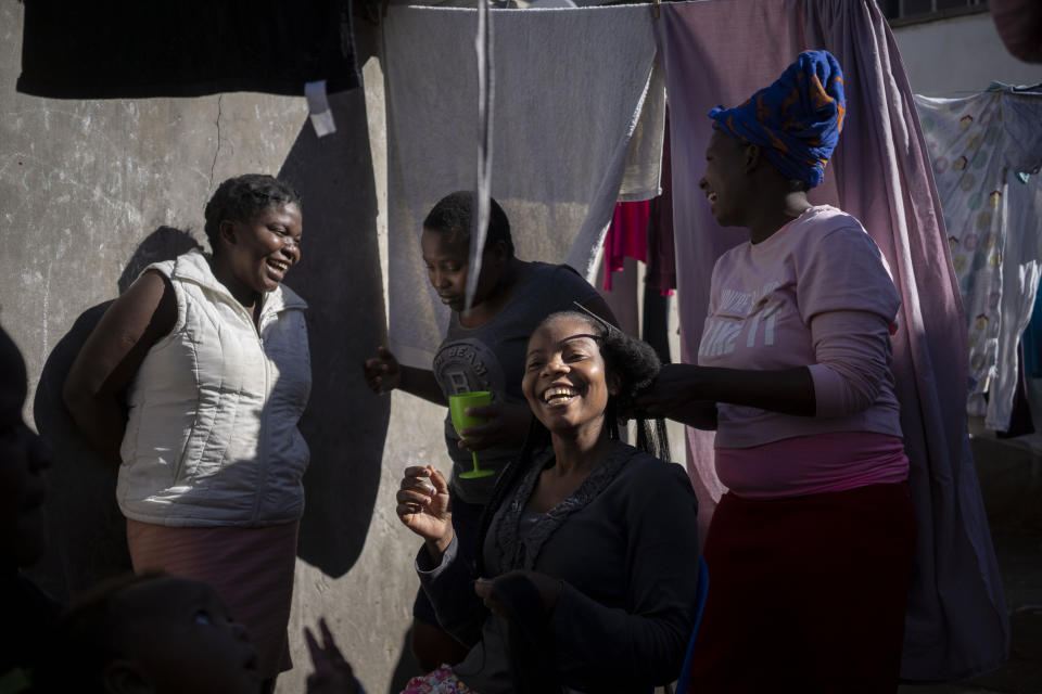 Fellowship Mukanhairi peina a su madre, una migrante zimbabueña ciega, en un barrio de Johannesburgo el 16 de abril del 2020. Varias personas sin tapabocas, muy cerca una de otra, ignoran las recomendaciones para combatir la propagación del coronavirus. (AP Photo/Bram Janssen)