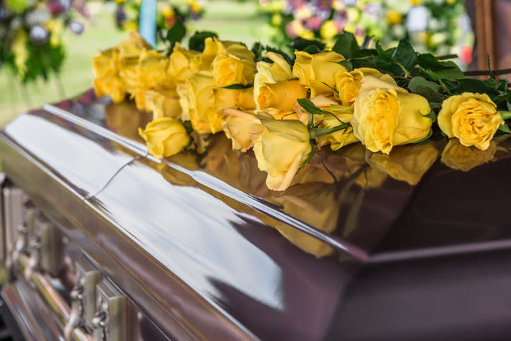 A casket adorned with yellow roses, surrounded by a floral display in an outdoor setting