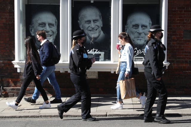 Police officers and members of the public walk past a gallery in Windsor High Street, containing pictures of the duke (Andrew Matthews/PA)