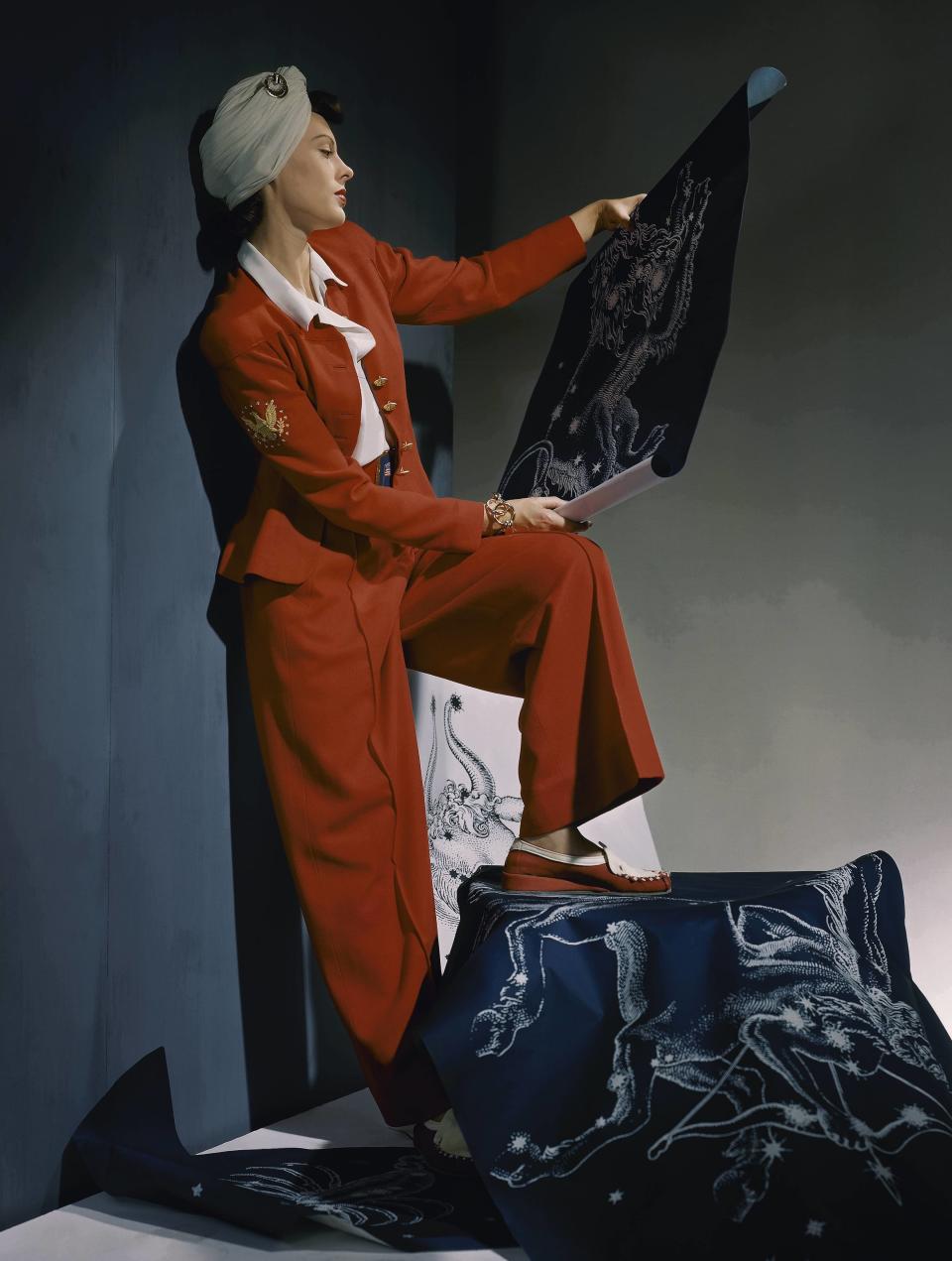 Mundy wears a red wool slack suit emblazoned with eagle figure, with white shirt and white turban, surrounded by mythological constellation illustrations in Vogue, 1940.&nbsp;