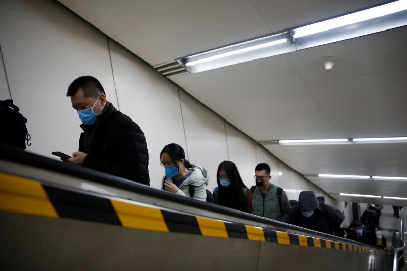 People wearing face masks ride an escalator as they exit a subway station following an outbreak of the coronavirus disease (COVID-19), in Beijing