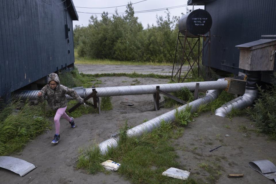 Leah Ekamrak runs past a plumbing pipeline between two village buildings, Sunday, Aug. 20, 2023, in Akiachak, Alaska. The arrival of indoor plumbing in an Alaska village is a godsend for residents who can now turn on a tap for their drinking water or start a machine to do their laundry. (AP Photo/Tom Brenner)
