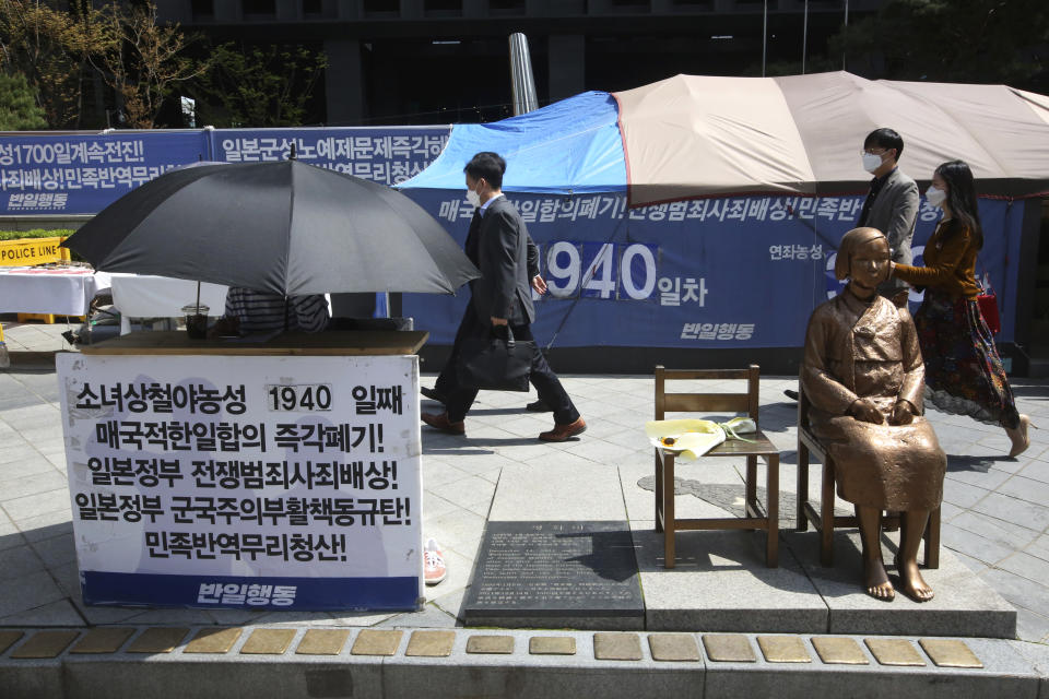 A protester under an umbrella sits next to a statue symbolizing a wartime sex slave to demand full compensation and an apology for them near Japanese Embassy in Seoul, South Korea, Wednesday, April 21, 2021. A South Korean court on Wednesday rejected a claim by South Korean sexual slavery victims and their relatives who sought compensation from the Japanese government over their wartime sufferings. The banner reads: "Apology and compensation." (AP Photo/Ahn Young-joon)