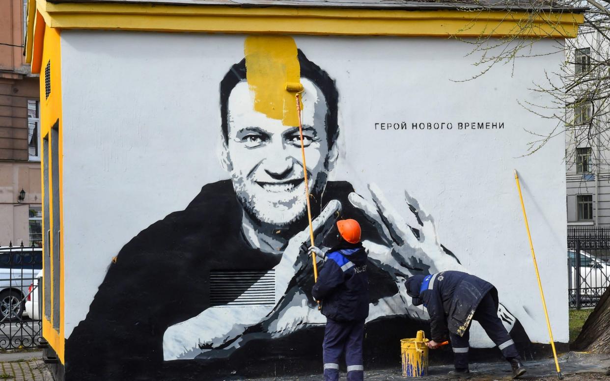 A worker paints over graffiti of jailed Kremlin critic Alexei Navalny in Saint Petersburg. The inscription reads: "The hero of the new times." - OLGA MALTSEVA /AFP