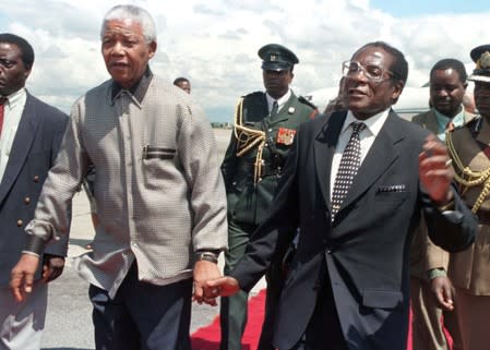 FILE PHOTO: President Robert Mugabe of Zimbabwe (R) holds hands with his South African counterpart Nelson Mandela greeting him on his arrival in the country