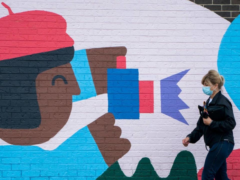 A woman in a mask walks past a mural as she makes her way to a grocery store in Gatineau, Que. (Adrian Wyld/The Canadian Press - image credit)