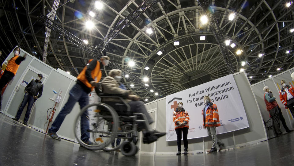 A person in a wheelchair is guided in a new coronavirus, COVID-19, vaccination center at the 'Velodrom' (velodrome-stadium) in Berlin, Germany, Wednesday, Feb. 17, 2021. (AP Photo/Michael Sohn, pool)