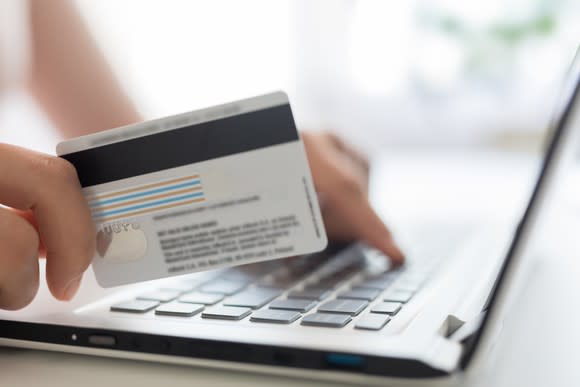 A person holds a credit card next to a laptop keyboard.