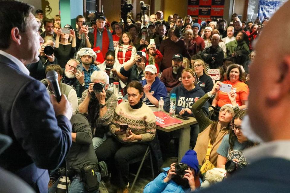 People listen as Florida Gov. Ron DeSantis, left, speaks during a rally on Saturday, Jan 13, 2023, at the Never Back Down super PAC headquarters in West Des Moines, IA.