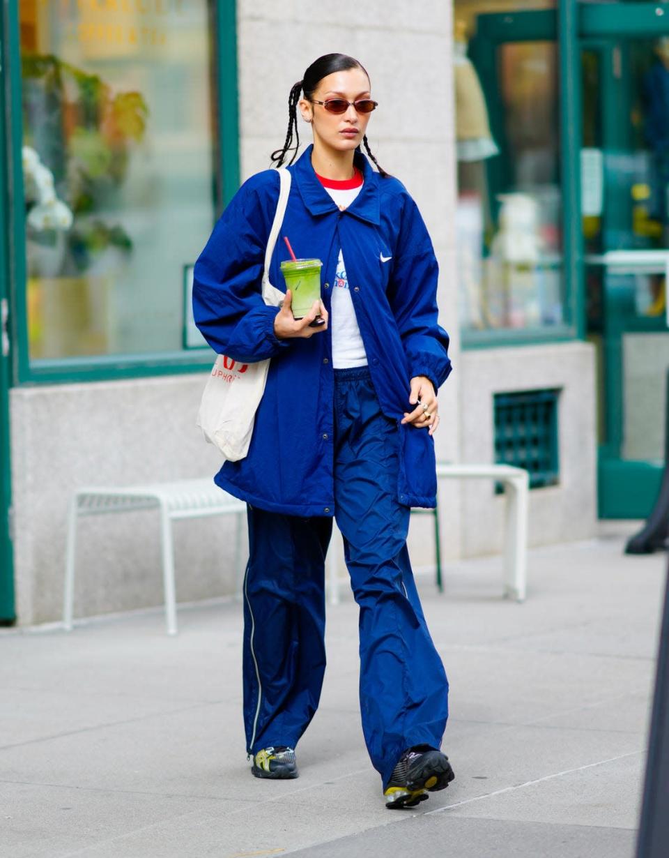 <p>The 25-year-old model looked as if she'd stepped out of a 1990s magazine during her outing in NYC on October 12. Carrying a green juice the model was seen walking through town in a blue Nike sports jacket and coordinated <a href="https://www.elle.com/uk/fashion/what-to-wear/articles/g31183/best-tracksuit-trousers-to-wear-to-work/" rel="nofollow noopener" target="_blank" data-ylk="slk:tracksuit" class="link ">tracksuit</a> bottoms, styled with trainers, a white tote bag, a white T-shirt with a green neckline, orange-tinted sunglasses and hair slicked back into pigtails and plaits. </p>