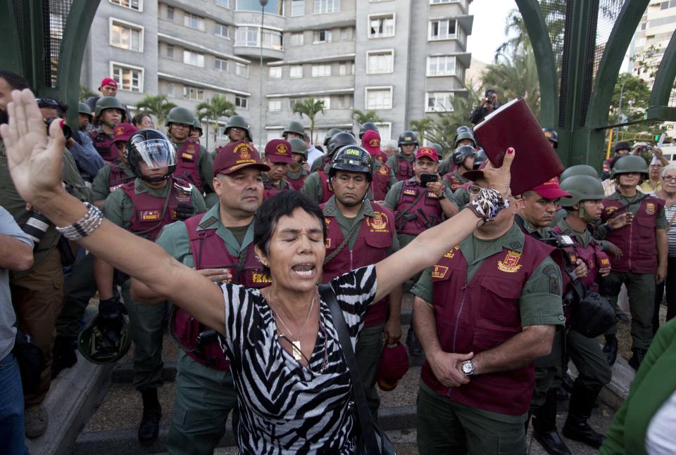 A woman prays with a bible in her hand, in front of Bolivarian National Guard officers during an anti-government protest in Plaza Altamira, Caracas, Venezuela, Tuesday, March 18, 2014. Protesters blocked the streets only when traffic lights turned red under the watchful gaze of the National Guard. Security forces have taken control of the plaza that has been at the heart of anti-government protests that have shaken Venezuela for a month. (AP Photo/Esteban Felix)