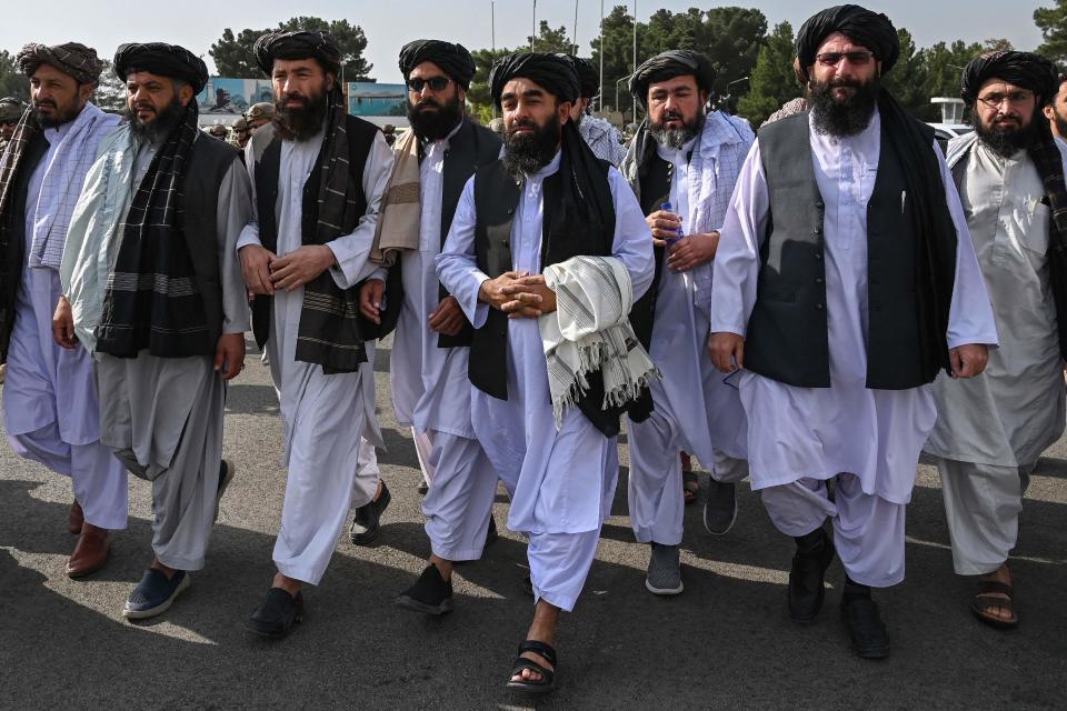 Taliban spokesman Zabihullah Mujahid, at center holding shawl, arrives accompanied by officials to address a media conference at the airport in Kabul on Aug. 31, 2021. The Taliban joyously fired guns into the air and offered words of reconciliation as they celebrated defeating the United States and returning to power after two decades of war that devastated Afghanistan.