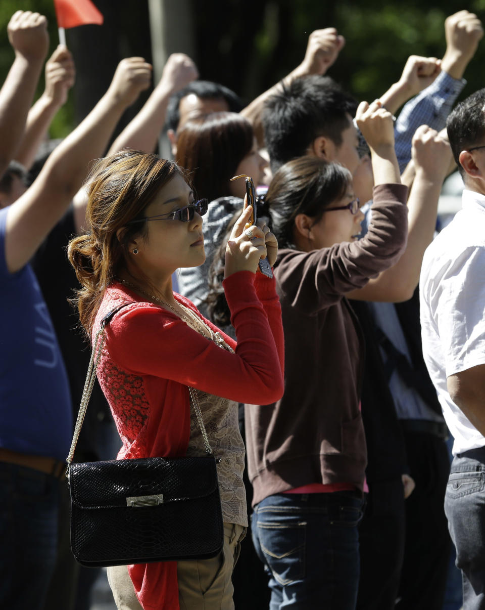 A Chinese woman uses her camera phone near protesters chant slogans outside the Japanese embassy in Beijing, China, Wednesday, Sept. 12, 2012. A territorial flare-up between China and Japan intensified as two Beijing-sent patrol ships arrived near disputed East China Sea islands in a show of anger over Tokyo's purchase of the largely barren outcroppings from their private owners. (AP Photo/Ng Han Guan)