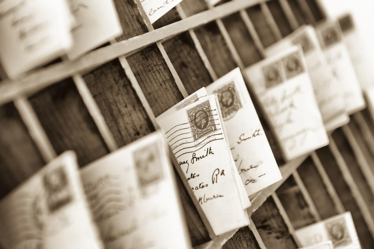 old fashioned letters and postcards sorted into old fashioned wooden mail box slots. 1930s postmarked British stamp at frame centre.