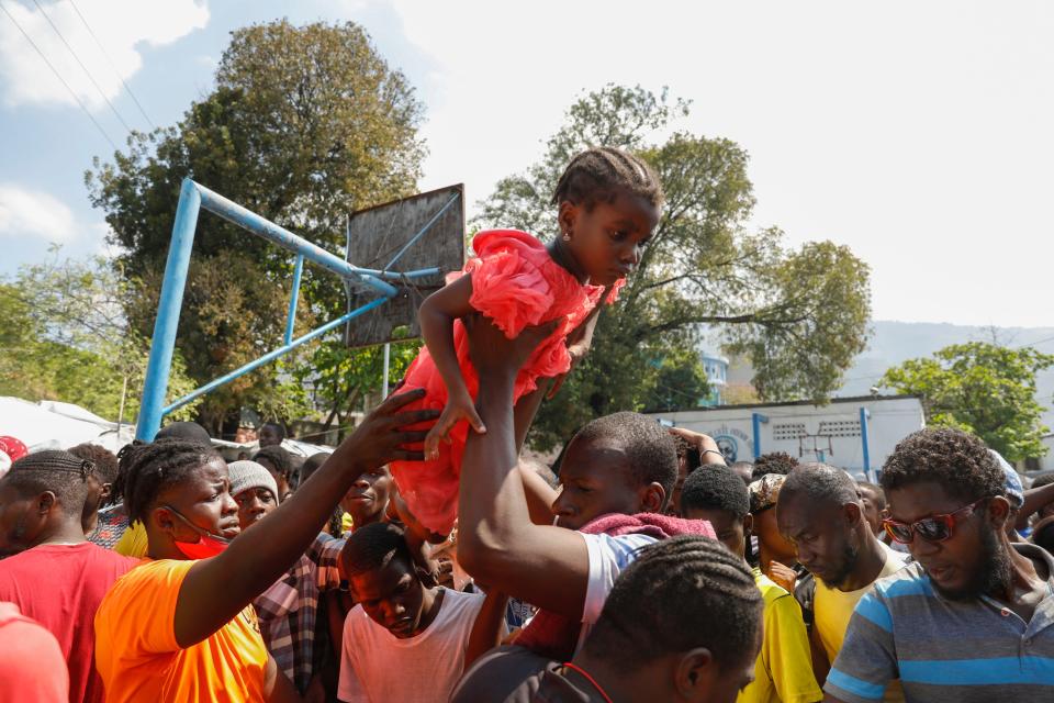 A father lifts his daughter to the front of a line of people waiting to receive a plate of food, at a shelter for families displaced by gang violence in Port-au-Prince, Haiti, Thursday, March 14, 2024. (AP Photo/Odelyn Joseph)