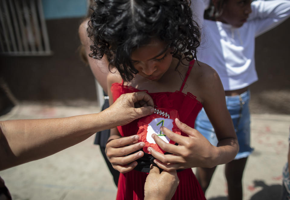 An organizer pins a #1 badge on Rosario Gutierrez, 11, after she was selected as child queen for the upcoming carnival festivities during a homespun beauty pageant, in the Antimano neighborhood of Caracas, Venezuela, Friday, Feb. 5, 2021. Neighborhood organizers said they’re trying to revive this carnival pageant tradition that’s been lost in recent years of economic and political crisis. (AP Photo/Ariana Cubillos)