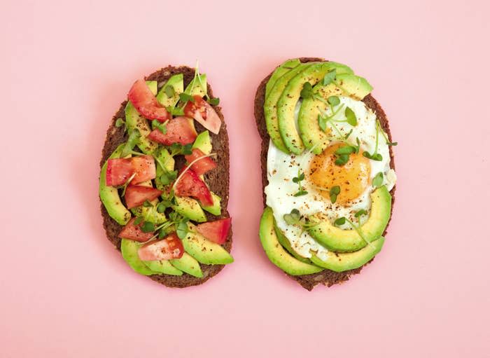 Two slices of avocado toast, one with tomatoes and the other topped with a fried egg