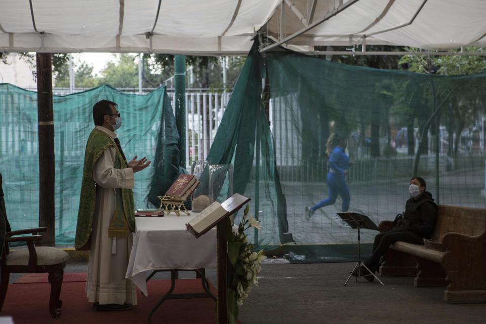 A runner jogs past as Rev. Adrian Vazquez celebrates an outdoor Mass held under a tent just outside the quake-damaged Our Lady of the Angels Catholic church, in the Guerrero neighborhood of Mexico City, Sunday, Aug. 7, 2022. Just weeks before the anniversary of the Sept. 19, 2017, quake, Vazquez announced to his parishioners that work is resuming on restoration of the Catholic temple. (AP Photo/Ginnette Riquelme)