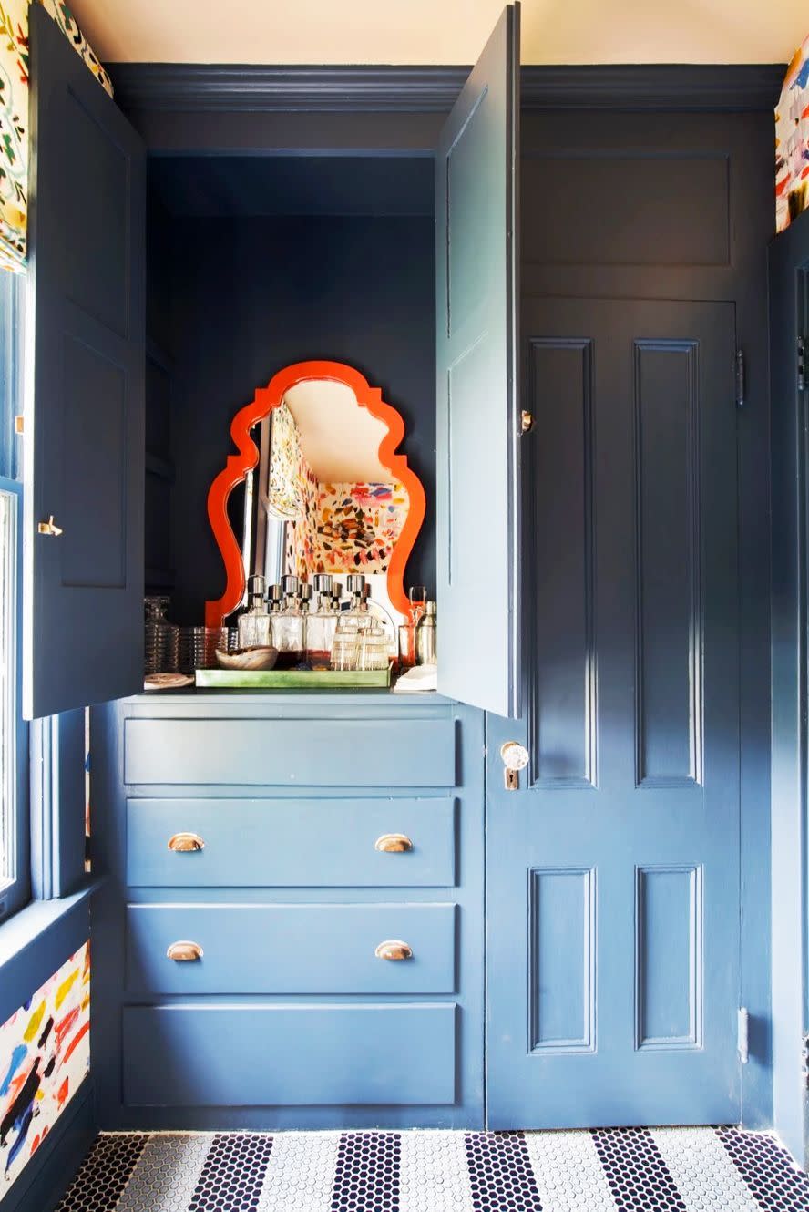 <p>This hidden vanity in bathroom designed by <a href="https://www.gaildavisdesignsllc.com/portfolio" rel="nofollow noopener" target="_blank" data-ylk="slk:Gail Davis;elm:context_link;itc:0;sec:content-canvas" class="link ">Gail Davis</a> is fun pop of surprising color. The orange mirror highlights the warmth of the curtains and vibrant wallpaper while the striped penny tile floor complements the navy paint and keeps things cool when the cabinets are closed. </p>