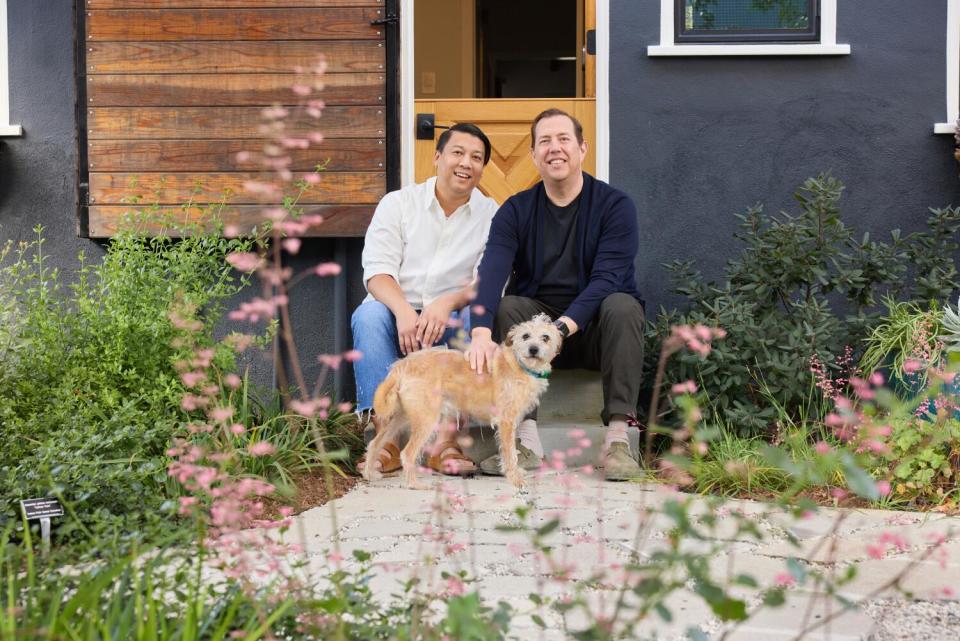 Two men and a dog sit on a step in their backyard