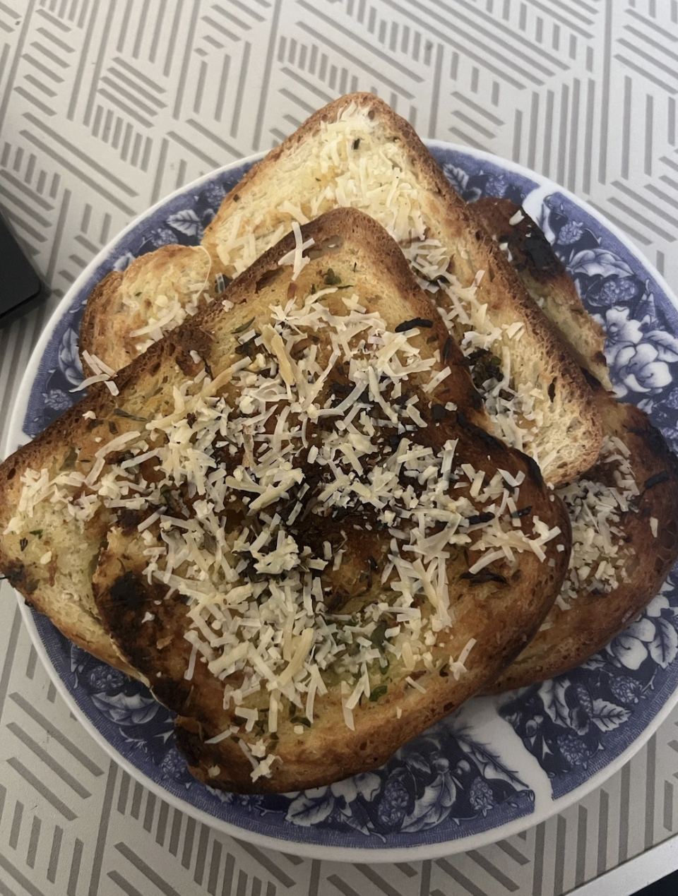 A plate with several slices of toasted bread, topped with shredded cheese and herbs. The plate has a decorative design