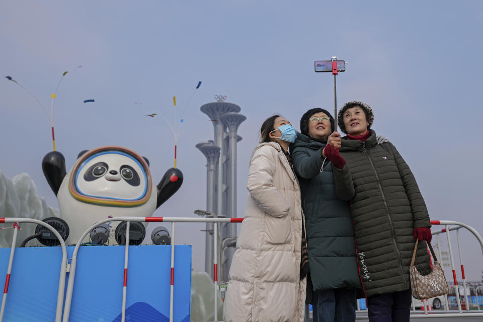 A woman wearing a face mask to help protect from the coronavirus takes a selfie with her companion against a Beijing Winter Olympics Mascot and Olympic Tower in Beijing, Wednesday, Jan. 19, 2022. China has locked down parts of Beijing's Haidian district following the detection of three cases, just weeks before the capital is to host the Winter Olympic Games. (AP Photo/Andy Wong)