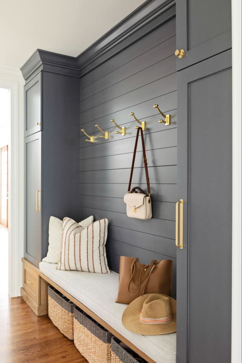Gray built in bench with cabinets and long white cushion, gold hooks