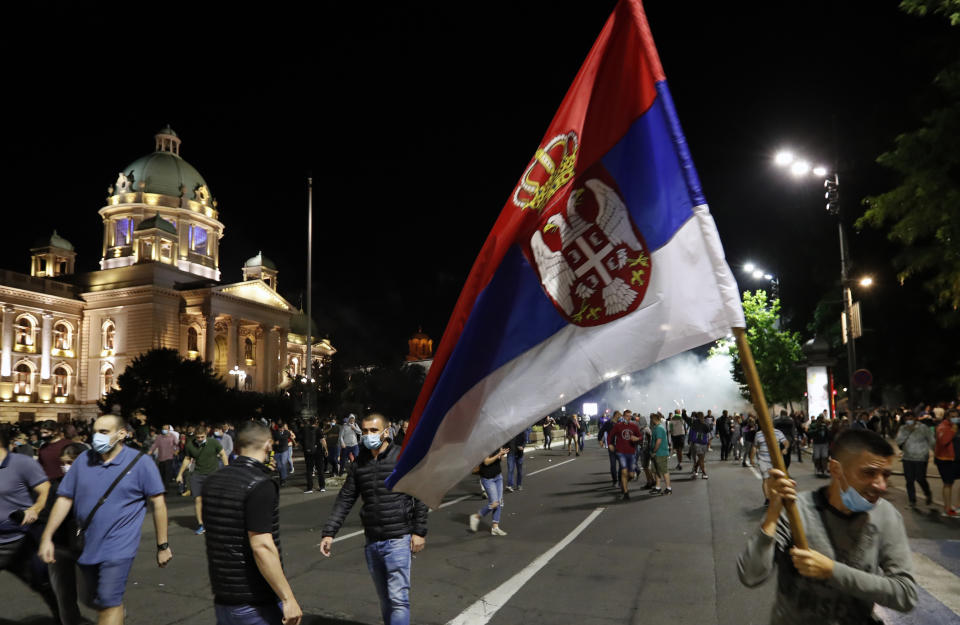 Protesters run from tear gas in front of Serbian parliament building in Belgrade, Serbia, Tuesday, July 7, 2020. Thousands of people protested the Serbian president's announcement that a lockdown will be reintroduced after the Balkan country reported its highest single-day death toll from the coronavirus Tuesday. (AP Photo/Darko Vojinovic)