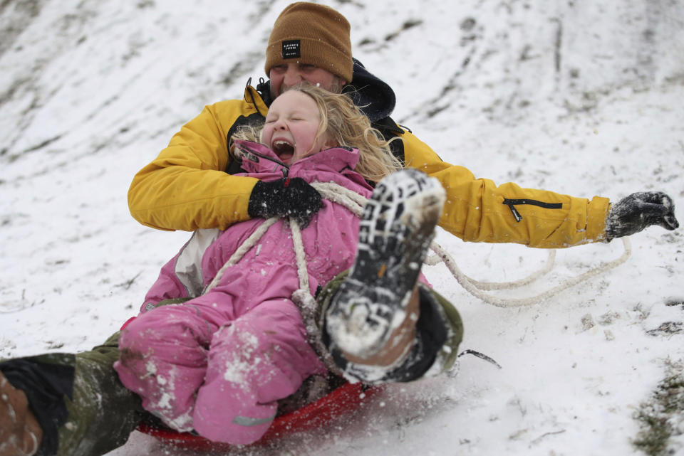 Adult and child during sledging play time near the seafront at Southend-on-Sea, south England, Monday Feb. 8, 2021, as people are still allowed out to exercise in their family bubbles . Schools are holding online lessons due to the coronavirus, and authorities have issued a severe weather warning for snow over the coming days, that will allow for more family play in the winter conditions. (Yui Mok/PA via AP)