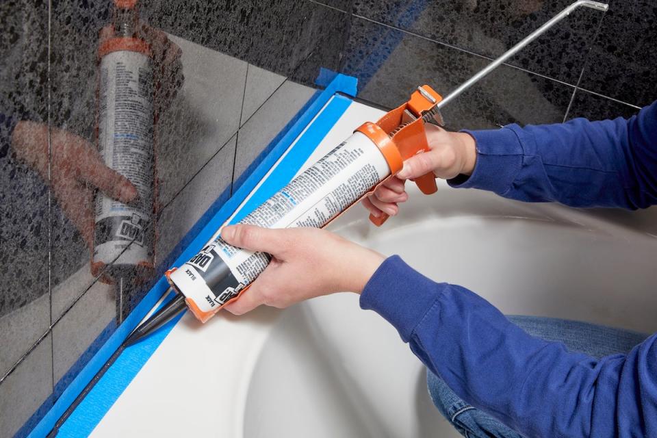 Woman caulking around a tub between rows of painter's tape.