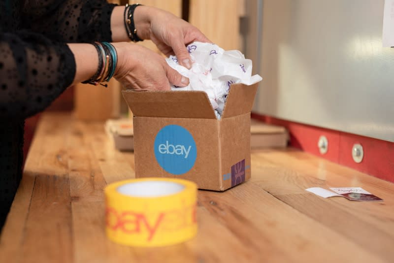 A person placing an item in an eBay branded carboard box.